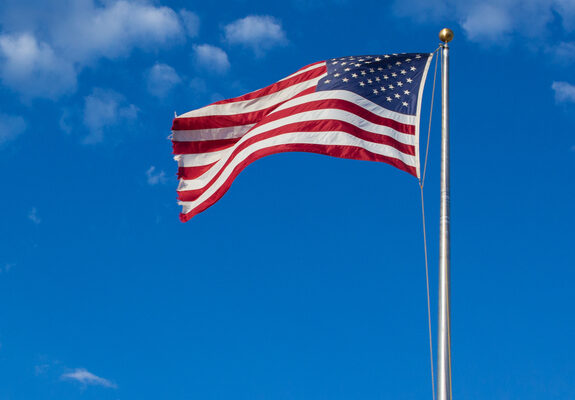 American flag - star and stripes floating over a cloudy blue sky