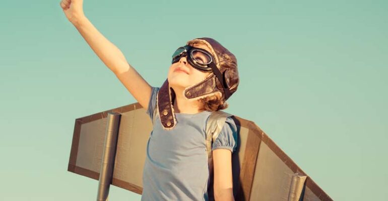 A young girl with plastic wings on her back, looking up at the sky