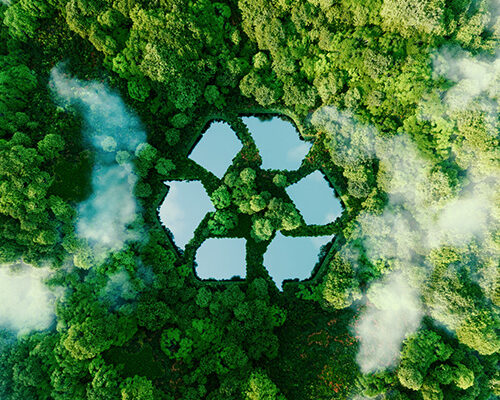A top down shot of a lush, green forest with whisps of white clouds. In the center of the image is a photoshopped series of ponds designed to look like the traditional "Recycling Arrow"