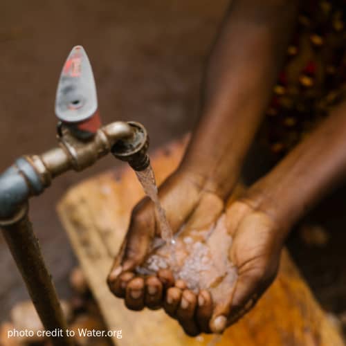 Water from a tap flows into a woman's cupped hands.